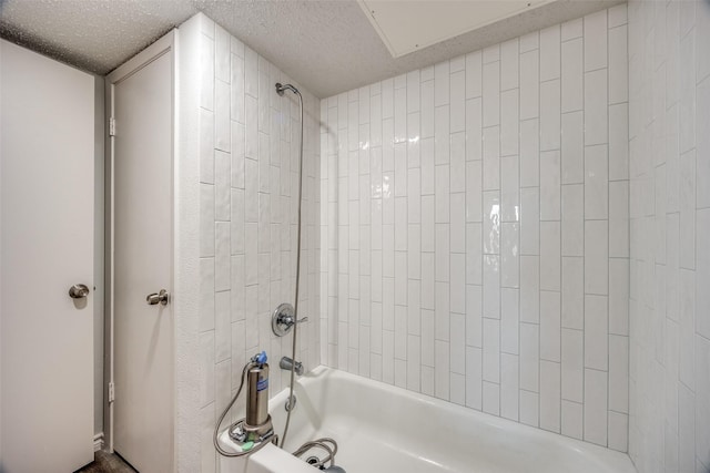 bathroom with a textured ceiling and tiled shower / bath