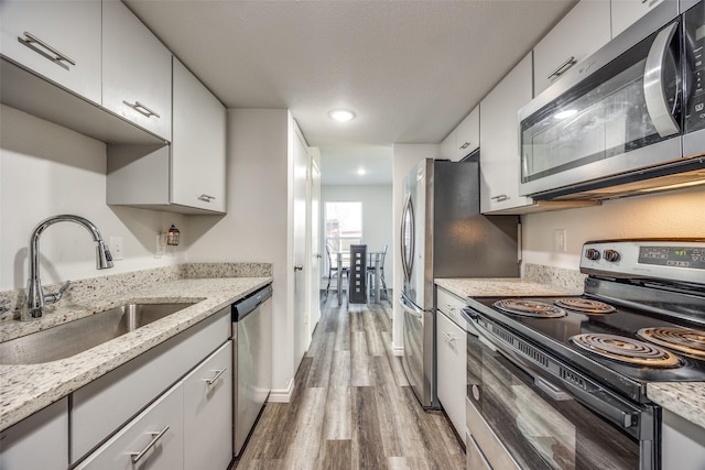 kitchen with white cabinets, appliances with stainless steel finishes, light stone counters, and sink