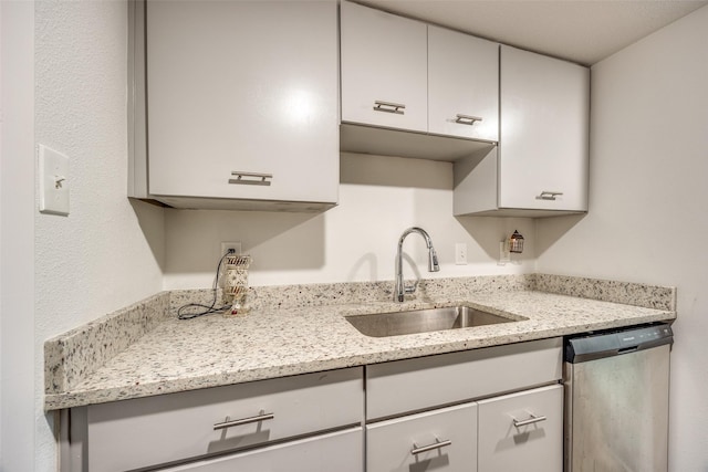 kitchen featuring dishwasher, light stone countertops, and sink