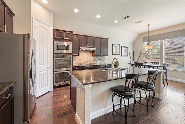 kitchen with stainless steel appliances, vaulted ceiling, sink, pendant lighting, and dark stone countertops