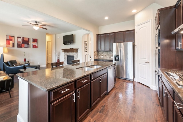 kitchen with tasteful backsplash, stainless steel appliances, sink, a fireplace, and an island with sink