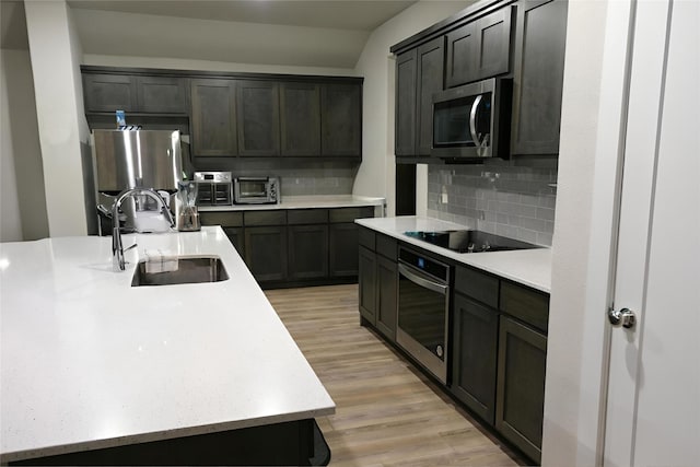 kitchen featuring appliances with stainless steel finishes, sink, decorative backsplash, a center island with sink, and light hardwood / wood-style flooring