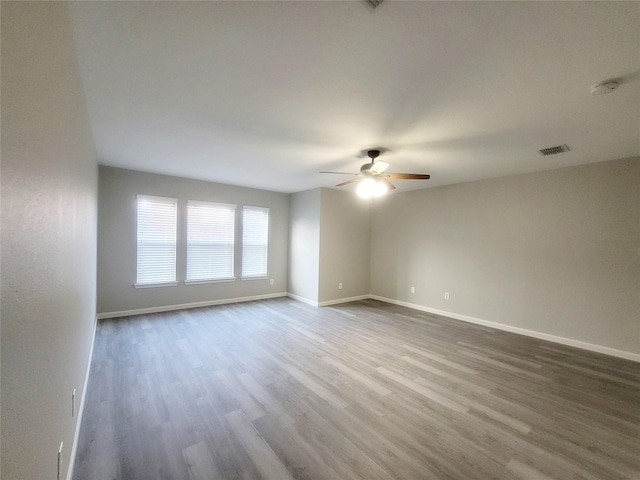 empty room featuring a ceiling fan, baseboards, visible vents, and wood finished floors