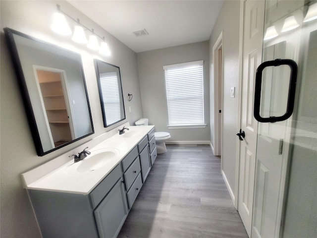 bathroom featuring double vanity, visible vents, toilet, a sink, and wood finished floors