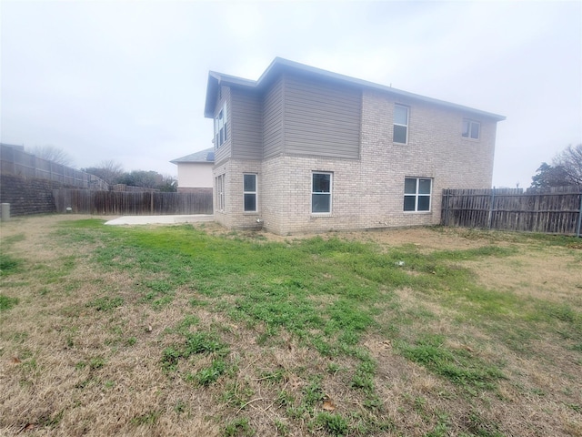 rear view of property featuring brick siding, a fenced backyard, and a yard