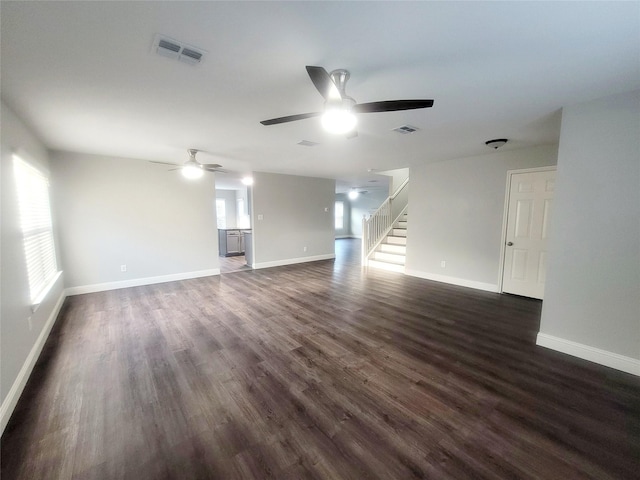 unfurnished living room with dark wood-style floors, stairway, visible vents, and baseboards