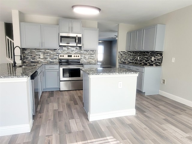 kitchen featuring stone countertops, appliances with stainless steel finishes, a sink, and gray cabinetry