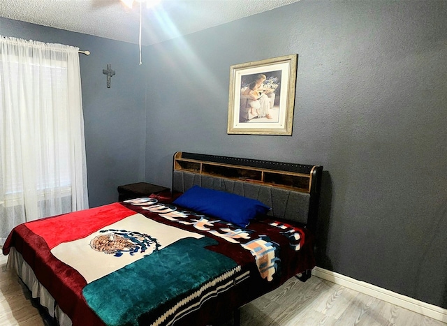 bedroom with ceiling fan, light wood-type flooring, and a textured ceiling