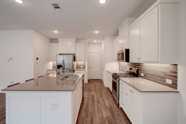 kitchen with sink, stainless steel appliances, backsplash, a kitchen island with sink, and white cabinets