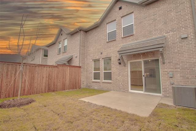 back house at dusk featuring a patio, central AC, and a lawn