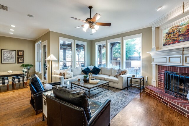 living room featuring ceiling fan, wood-type flooring, crown molding, and a brick fireplace