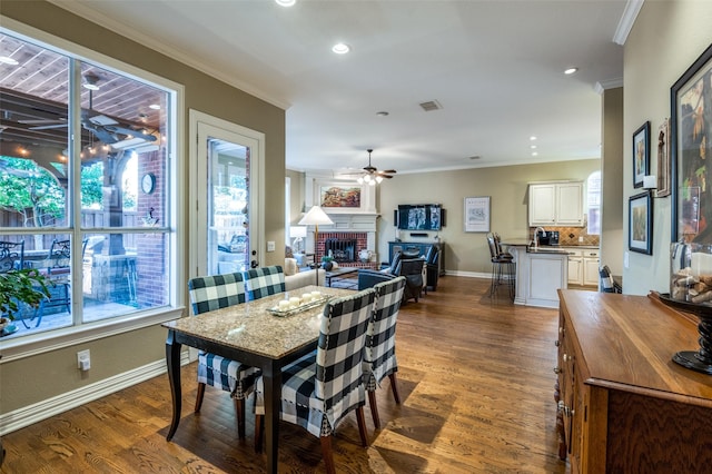 dining area with crown molding, ceiling fan, a fireplace, and dark wood-type flooring