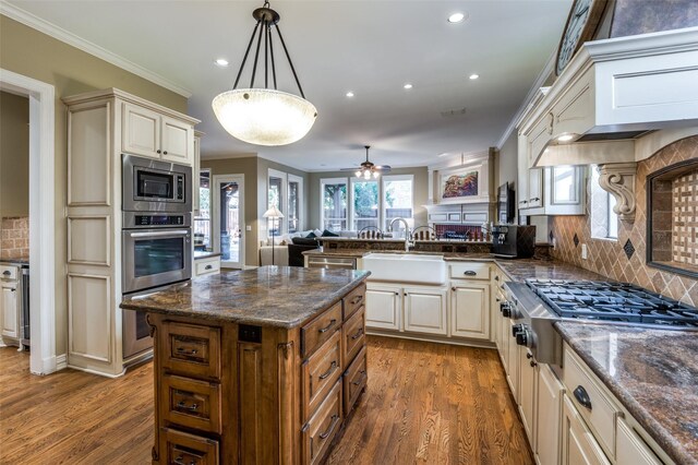 kitchen featuring stainless steel appliances, hanging light fixtures, backsplash, crown molding, and wood-type flooring