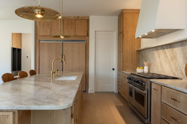 kitchen with sink, high end appliances, light stone counters, custom range hood, and a center island with sink