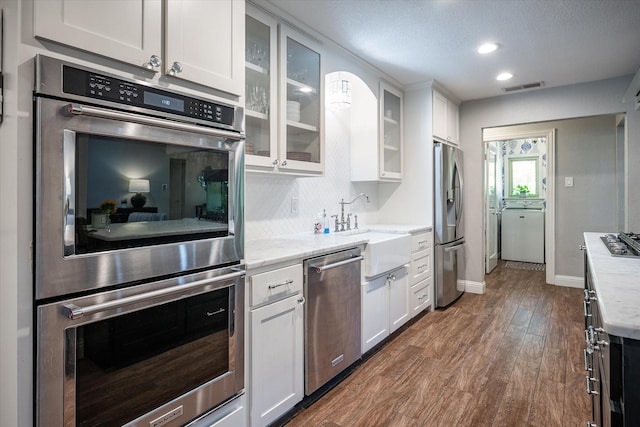 kitchen with dark wood-type flooring, appliances with stainless steel finishes, tasteful backsplash, light stone counters, and white cabinetry