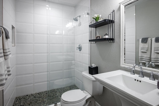 bathroom with a tile shower, sink, and toilet