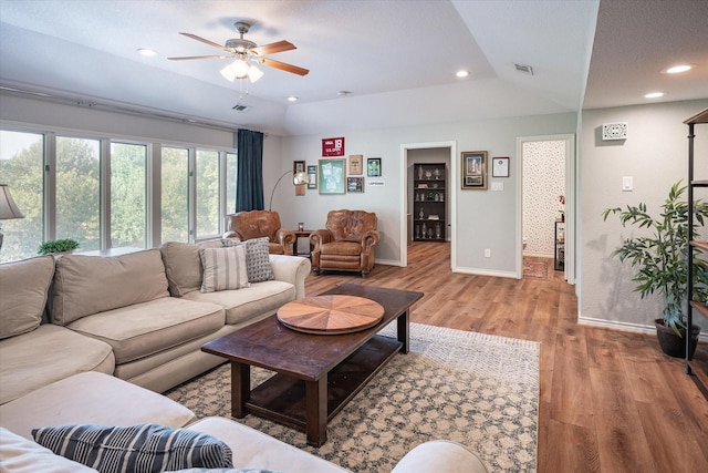 living room with a textured ceiling, vaulted ceiling, a raised ceiling, ceiling fan, and light hardwood / wood-style floors