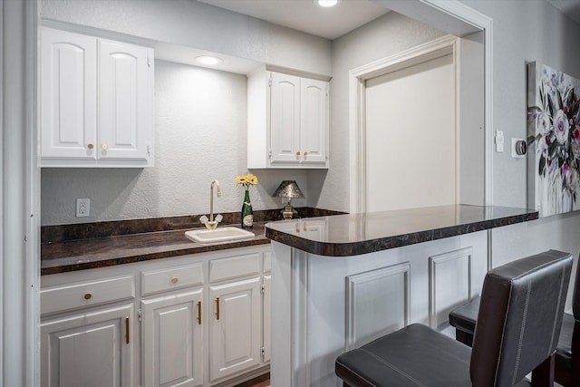 kitchen with a kitchen bar, kitchen peninsula, sink, and white cabinets