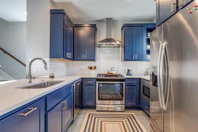 kitchen featuring sink, blue cabinetry, appliances with stainless steel finishes, decorative backsplash, and wall chimney exhaust hood