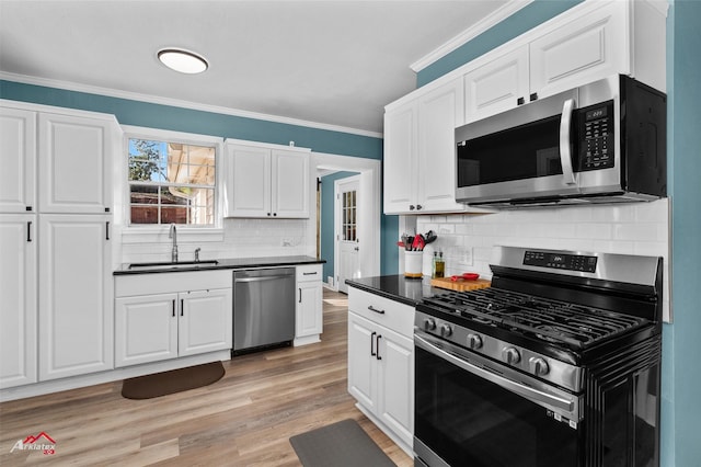 kitchen featuring appliances with stainless steel finishes, light wood-type flooring, ornamental molding, sink, and white cabinets