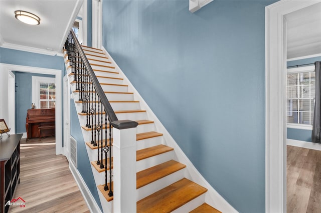 staircase with hardwood / wood-style floors, crown molding, and a healthy amount of sunlight