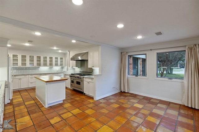 kitchen featuring white cabinets, double oven range, wall chimney range hood, and backsplash