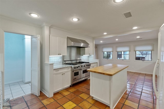 kitchen with double oven range, backsplash, wooden counters, white cabinets, and wall chimney exhaust hood