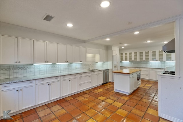 kitchen featuring appliances with stainless steel finishes, crown molding, wall chimney range hood, white cabinets, and a kitchen island