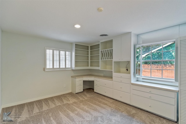 unfurnished office featuring built in desk, light colored carpet, and a healthy amount of sunlight