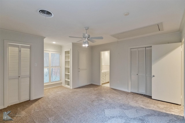 unfurnished bedroom with ceiling fan, crown molding, ensuite bathroom, light carpet, and two closets