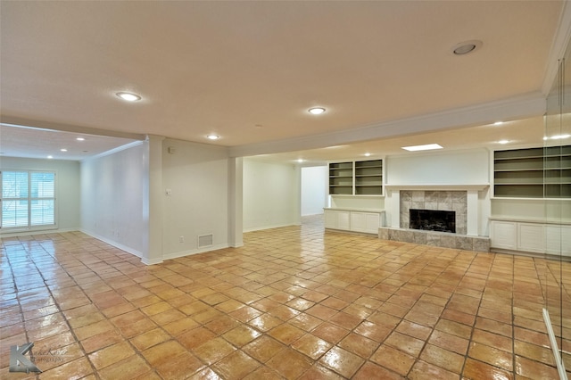 unfurnished living room featuring a tile fireplace, built in shelves, light tile patterned floors, and ornamental molding