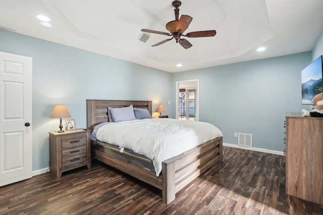 bedroom with ceiling fan, dark hardwood / wood-style flooring, and a tray ceiling