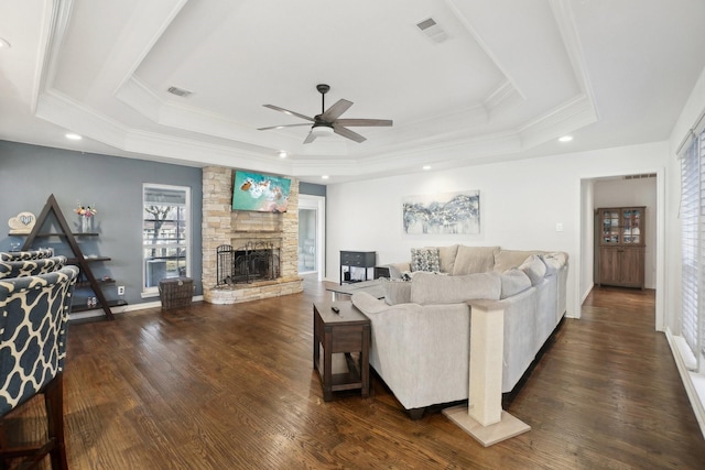 living room featuring dark hardwood / wood-style floors, a fireplace, a tray ceiling, and crown molding