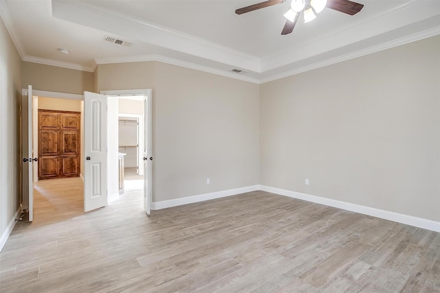 empty room with crown molding, ceiling fan, a tray ceiling, and light hardwood / wood-style floors