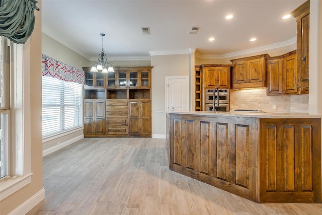 kitchen with light hardwood / wood-style flooring, ornamental molding, a notable chandelier, stainless steel double oven, and backsplash