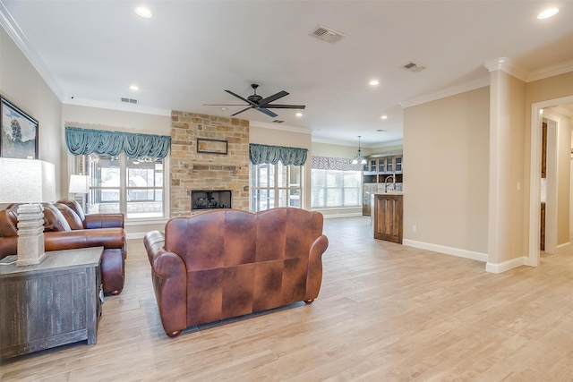 living room featuring ceiling fan, ornamental molding, a stone fireplace, and light wood-type flooring