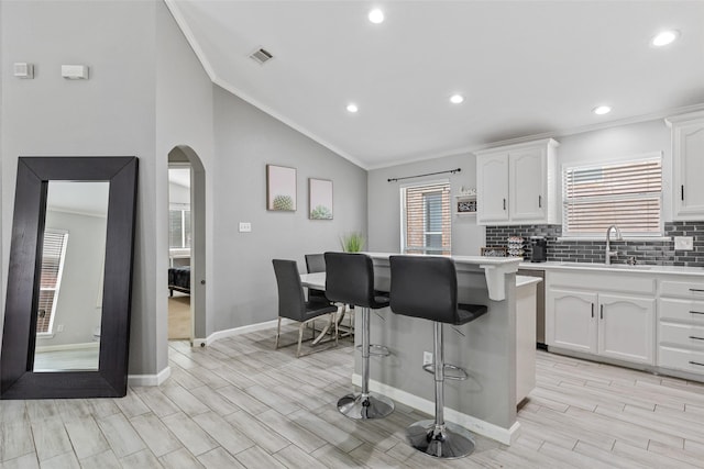 kitchen featuring a center island, white cabinets, crown molding, vaulted ceiling, and decorative backsplash