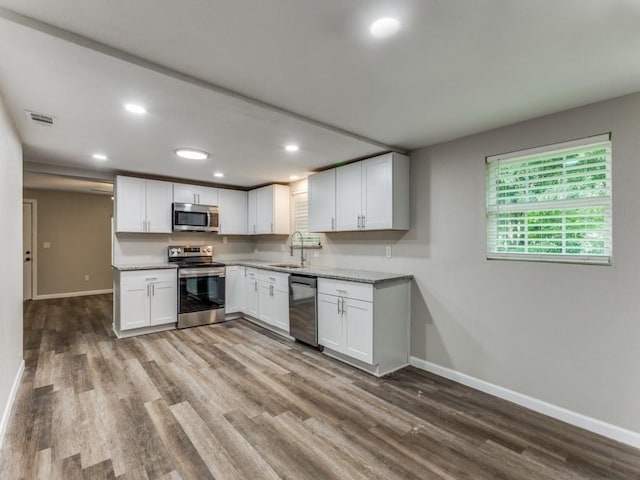 kitchen with hardwood / wood-style floors, sink, white cabinets, stainless steel appliances, and light stone countertops