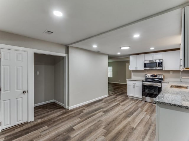 kitchen featuring sink, appliances with stainless steel finishes, white cabinetry, light stone countertops, and light wood-type flooring