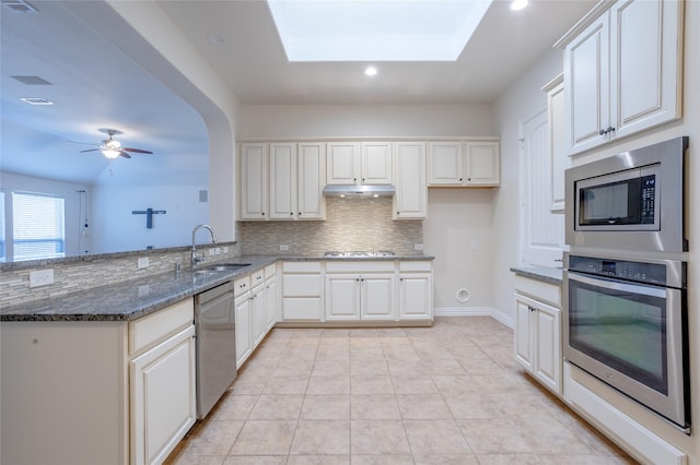 kitchen with dark stone counters, sink, a skylight, white cabinetry, and stainless steel appliances