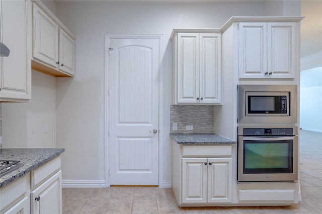 kitchen featuring light tile patterned floors, light stone countertops, appliances with stainless steel finishes, tasteful backsplash, and white cabinetry