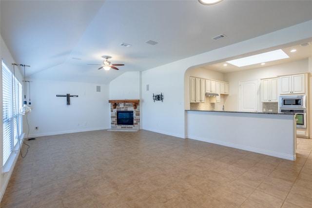 unfurnished living room featuring ceiling fan, a stone fireplace, and vaulted ceiling