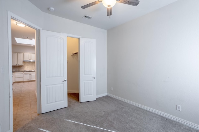 unfurnished bedroom featuring light carpet, a skylight, ceiling fan, a spacious closet, and a closet