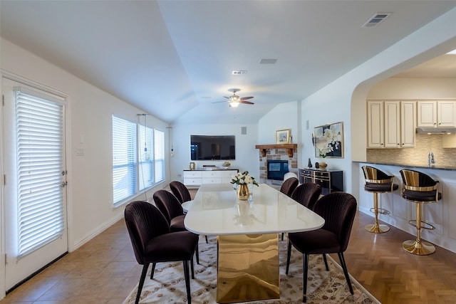 dining space featuring ceiling fan, a stone fireplace, and vaulted ceiling