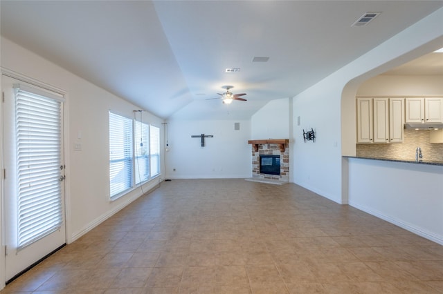 unfurnished living room with ceiling fan, lofted ceiling, a fireplace, and light tile patterned floors