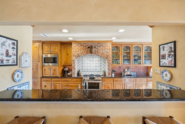 kitchen featuring decorative backsplash, a kitchen bar, dark stone countertops, and appliances with stainless steel finishes