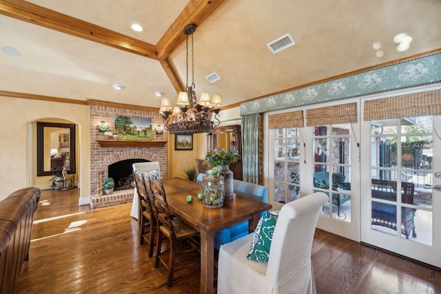 dining room with lofted ceiling with beams, an inviting chandelier, dark hardwood / wood-style floors, and a brick fireplace