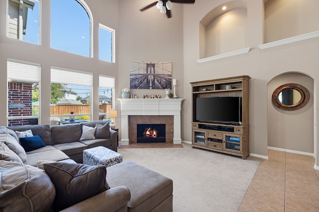 living room featuring tile patterned floors, a tiled fireplace, ceiling fan, and a high ceiling