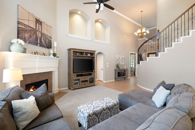 living room featuring ceiling fan with notable chandelier, crown molding, a high ceiling, and a tiled fireplace