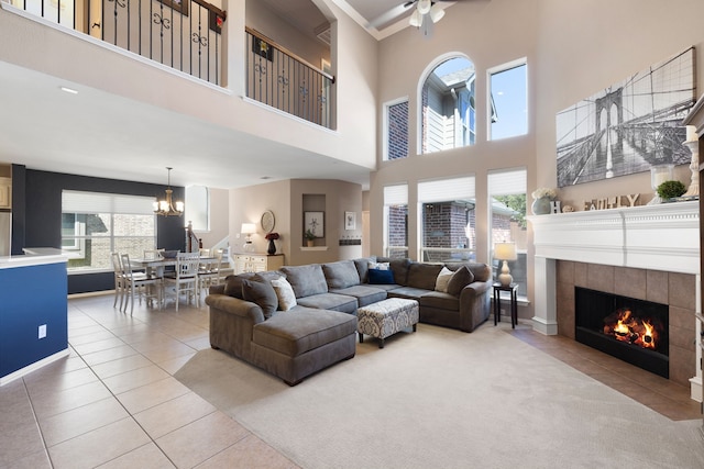 tiled living room featuring a fireplace, a towering ceiling, and ceiling fan with notable chandelier